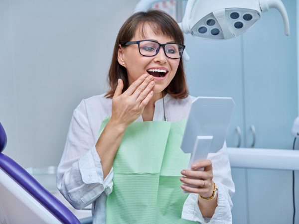 Woman smiling with hand on mouth, holding mirror.
